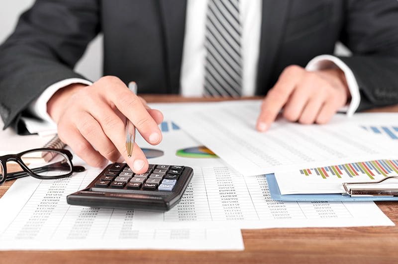 Hands on a calculator over printed financial reports